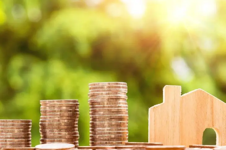 pièces de monnaie empilées et maison en bois symbolisant l'investissement immobilier fractionné