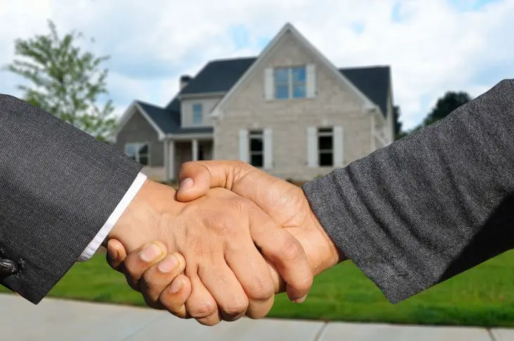 deux agents immobiliers se serrent la main devant une maison neuve