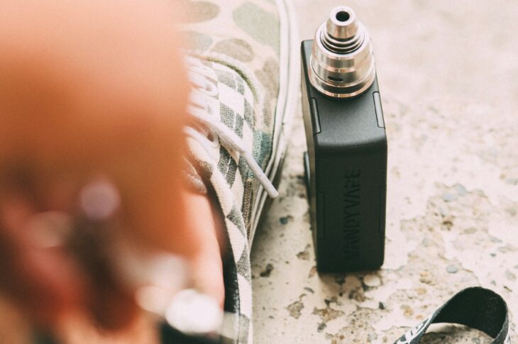 vaporisateur électronique noir avec atomiseur et lanyard sur surface sableuse